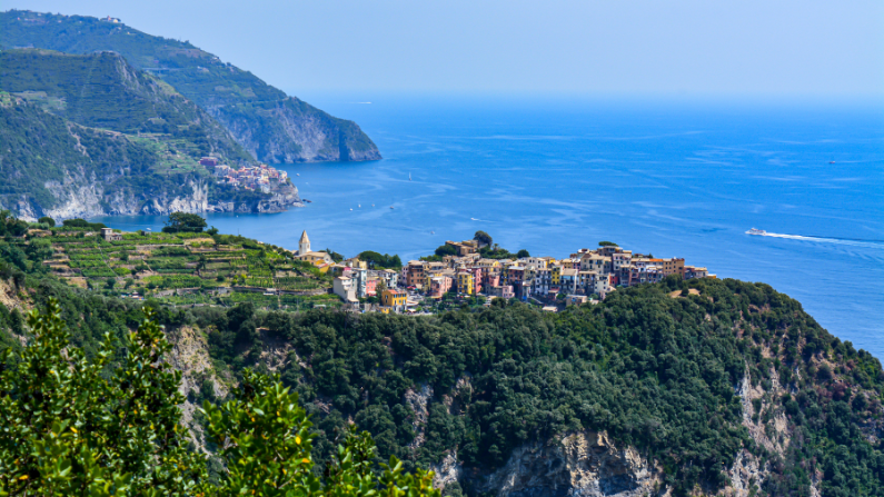 A colorful town of Corniglia, one of the five Cinque Terre towns, perched on a cliff surrounded by land, vineyards and craggy coastline overlooking blue ocean waters