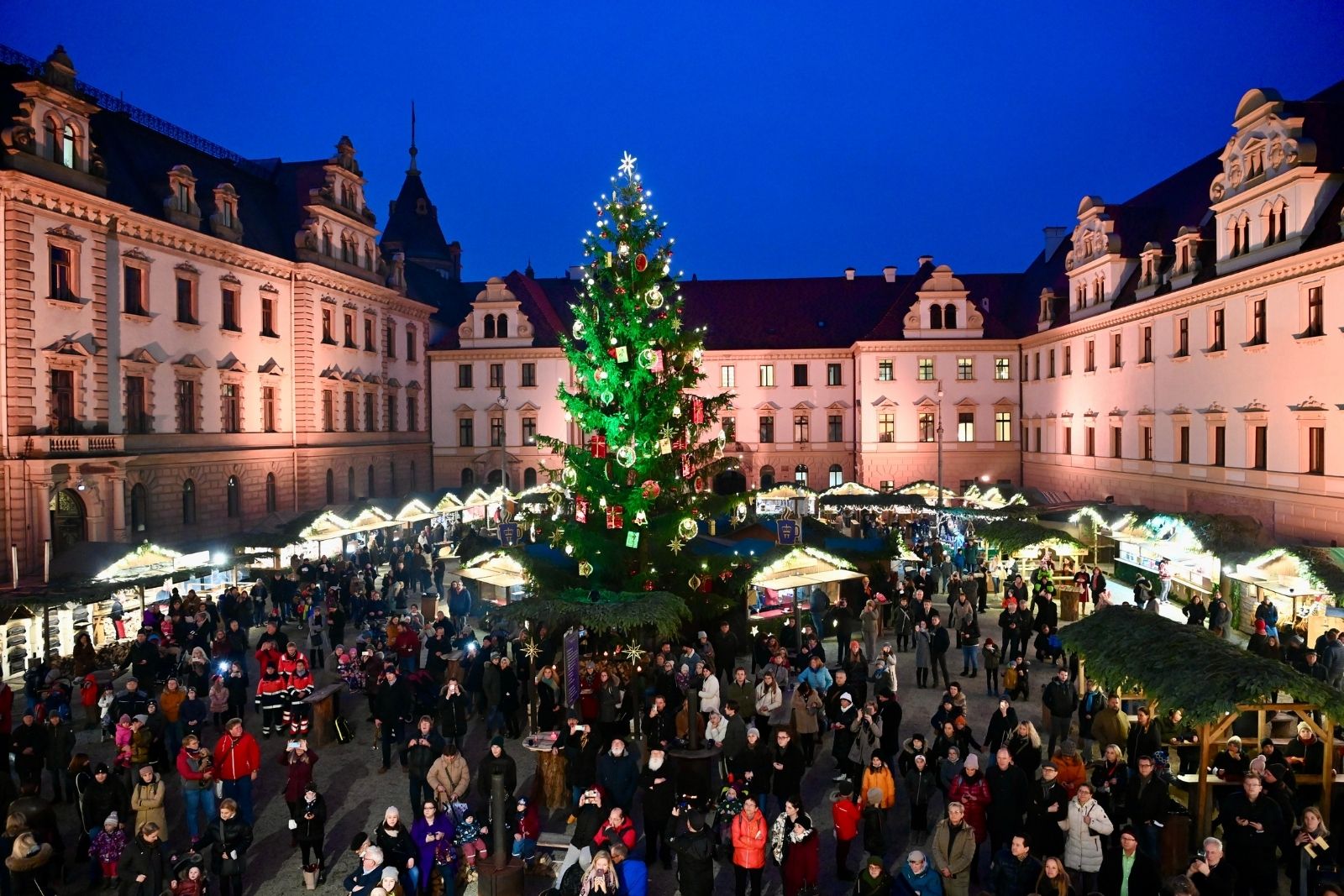A brightly lit Christmas market at night in a castle courtyard with a large christmas tree in the middle.