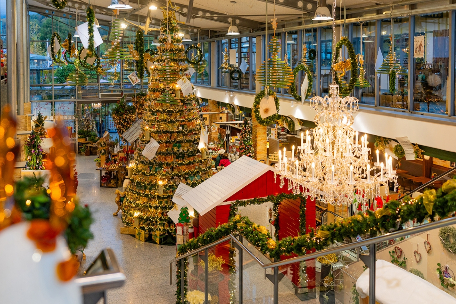 In a large gallery, there is a large Christmas tree made of glass bottles and surrounded by Christmas lights and decorations.